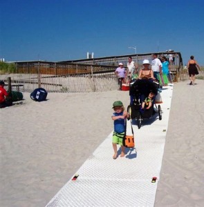 Photo of a mother with a pushchair walking on GroundGuards trackway mats laid on the beach to create an easily accessible pathway over sand.